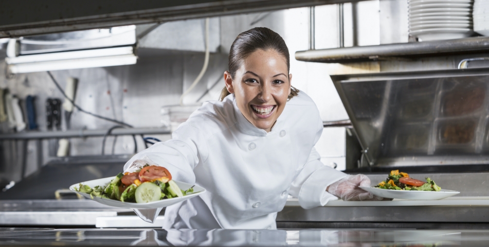 Female Hispanic chef (30s) in commercial kitchen, preparing gourmet salad.