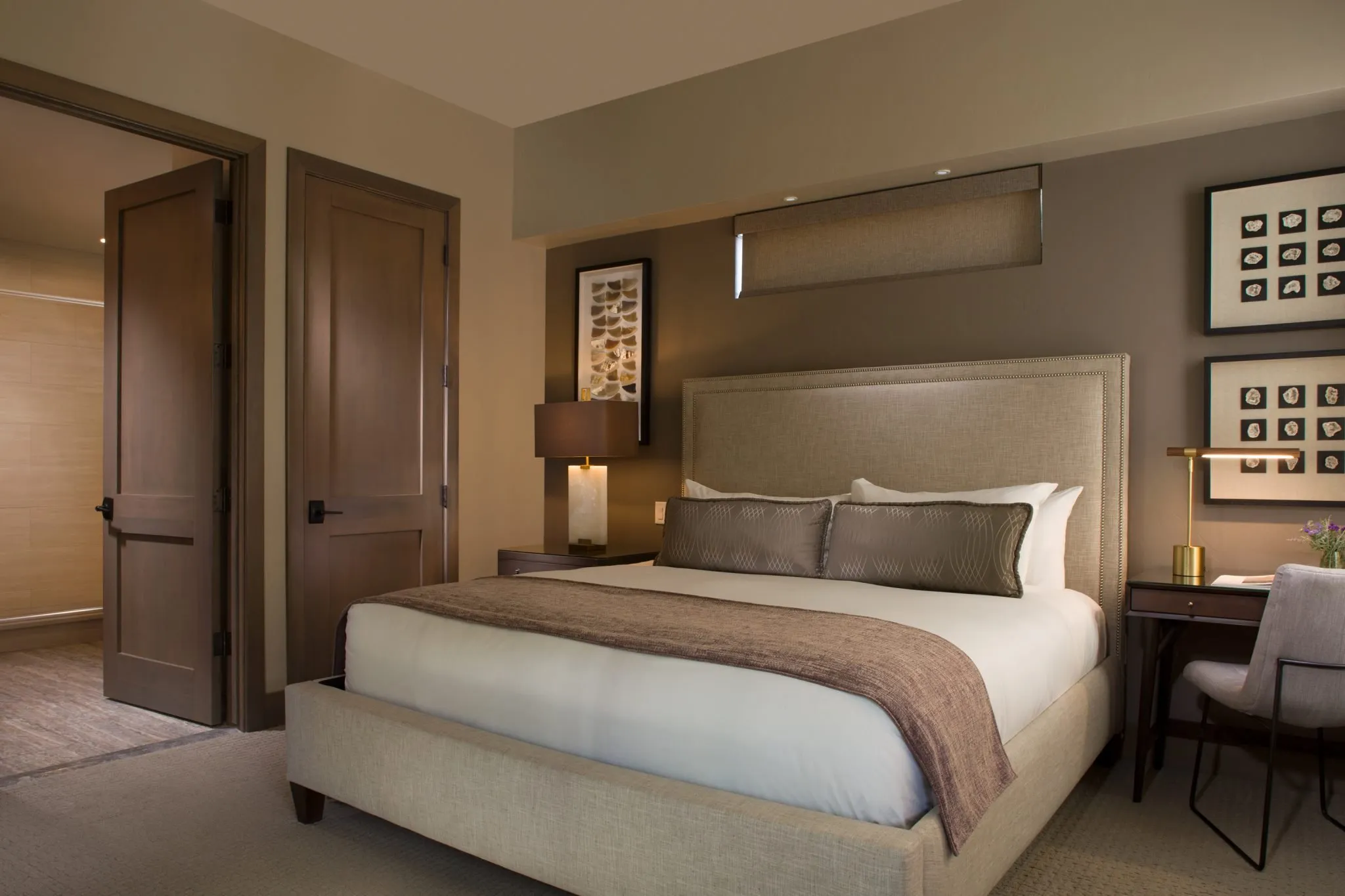 A luxurious hotel room with a large bed, desk, and artwork