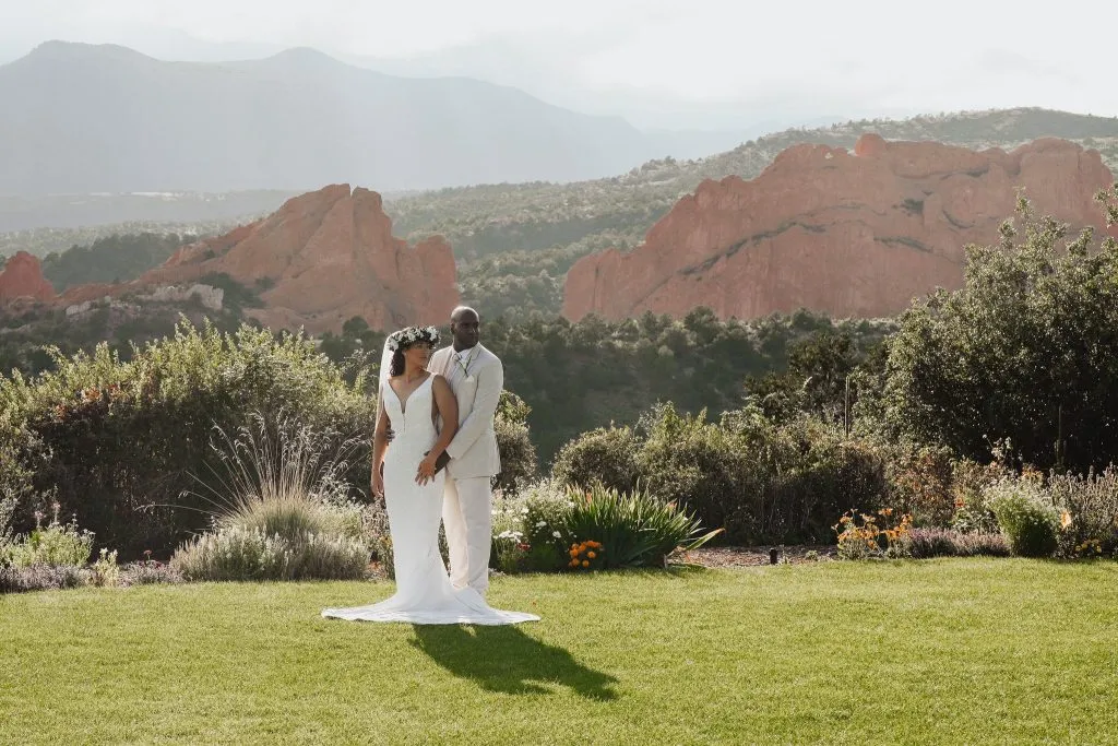 Couple posing on a green lawn with red rocks and mountain views at a Colorado Springs wedding venue.