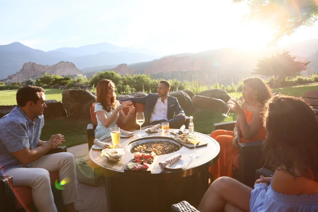 Coworkers gathering around an outdoor fire pit with drinks and appetizers for outdoor company retreat ideas.
