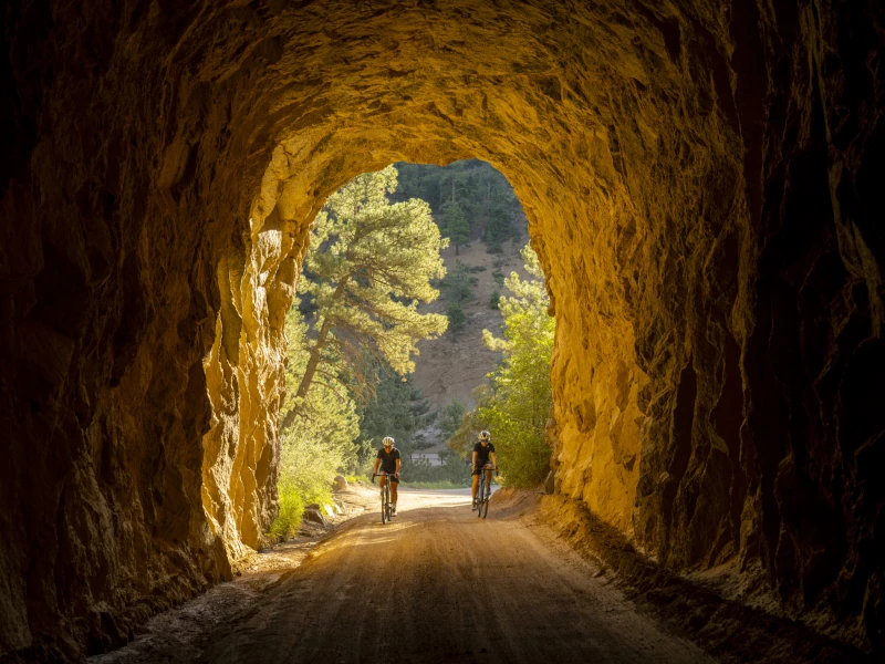 Two cyclists riding bikes through a natural carved rock tunnel