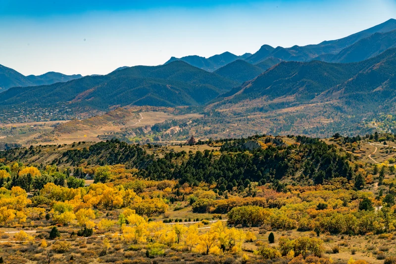 High-angle landscape view of golden autumn trees spreading toward mountain peaks