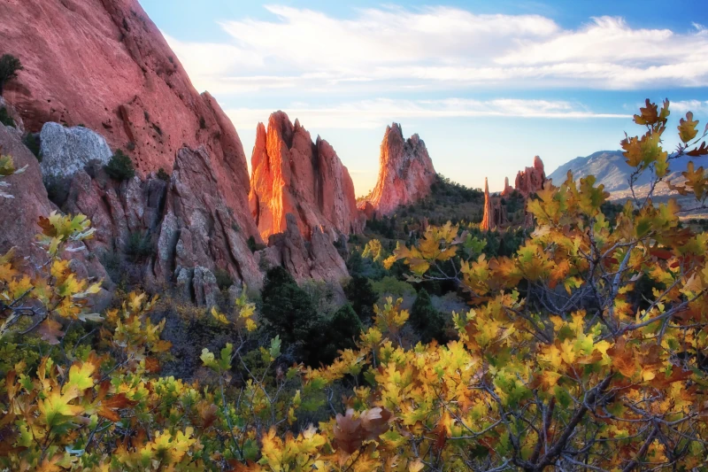 Sunrise glow illuminating red sandstone rock fins framed by golden oak leaves in autumn